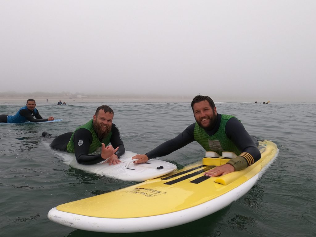 drei Surfer im Wasser, in die Kamera lachend